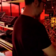 man playing synthesizer with other keyboards and synths on shelves